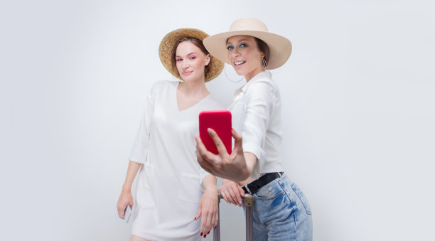 两个漂亮的女孩在旅行前对着白墙自拍，旅游概念图片下载