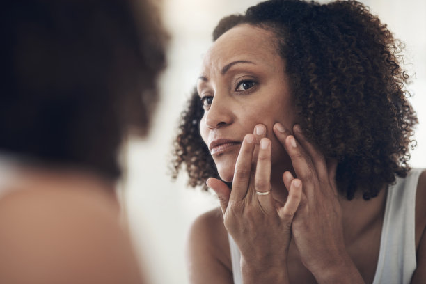 一个迷人的年轻女子站在她家里的浴室里，用镜子检查她的皮肤图片下载