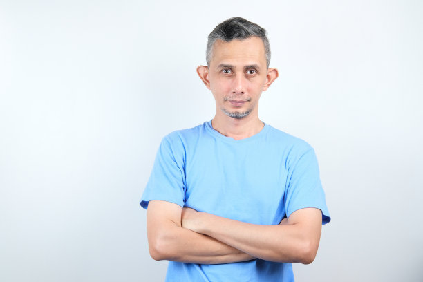 一个英俊的亚洲男人的肖像与蓝色的t恤折叠双臂。图片下载