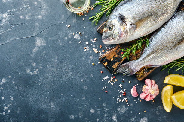 生鲜剑鱼或海鲷，配料为柠檬，百里香，大蒜，樱桃番茄和盐，在黑色石板，石头或混凝土背景。顶部视图与复制空间。图片下载