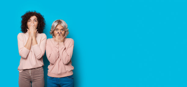 一头卷发的姐妹们惊讶地站在工作室的蓝色墙壁上，用手遮住了她们的嘴图片下载