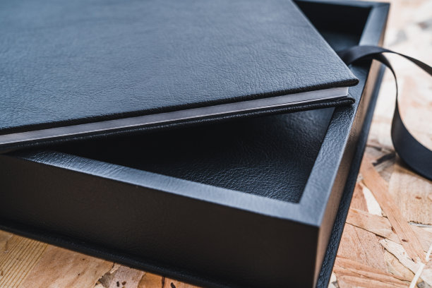 黑色皮革相册在桌子上与复古的木材背景。婚礼或家庭相册的回忆。家庭价值的记忆。图片下载