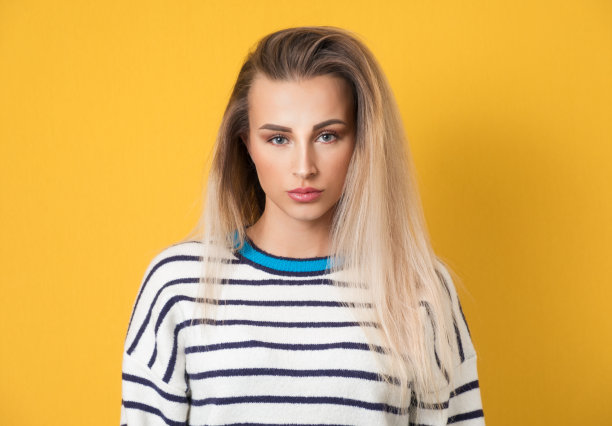 严肃的年轻女子看着相机，黄色背景上的孤立。一个美丽的女孩的正面视图肖像图片下载