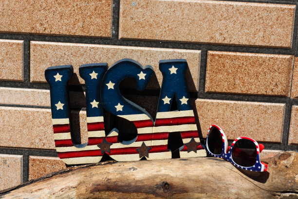 4 . 7月庆祝点子。在一个阳光明媚的日子里，在砖墙前的木质表面上，印有美国国旗颜色的美国字母和太阳镜图片下载