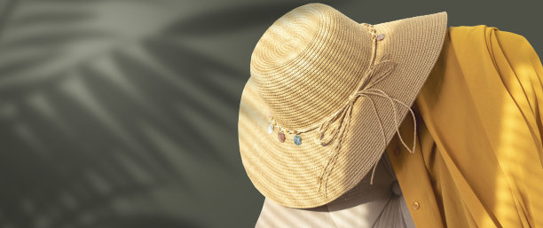 一种有黄色披风的柳条帽子，放在软垫椅的靠背上。平滑，单色墙壁背景。热带树叶的阴影。横幅。适合在海上休闲的夏日衣橱。图片下载