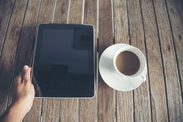 俯视图人手放在头顶的办公桌上笔记本电脑，咖啡杯放在木桌上复印空间。桌面笔记本电脑，笔记本电脑，咖啡杯，警官显示空白的木制背景。在家工作。图片下载