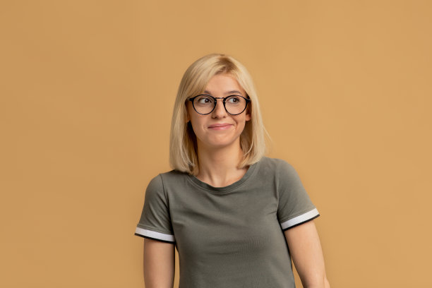 戴着眼镜的沉思女人思考问题，抚摸下巴，看向别处，米色背景图片下载