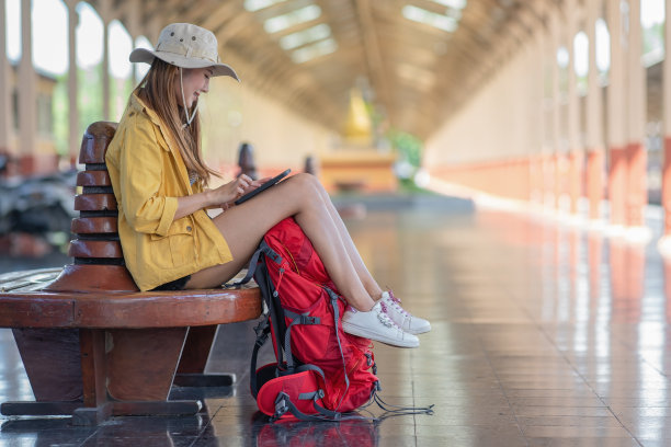 年轻女性背包客在站台上用平板电脑等车的照片图片下载
