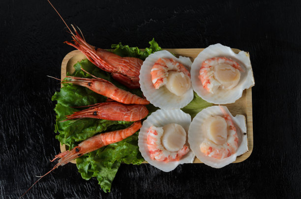 天然生扇贝和煮虾在水池和生菜叶在一个木碗在黑暗的背景。图片下载