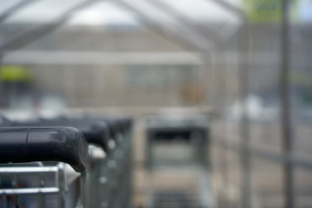 有黑色把手的购物车的一部分。手推车在一个玻璃屋顶下，位于超市前面。在德国。图片下载