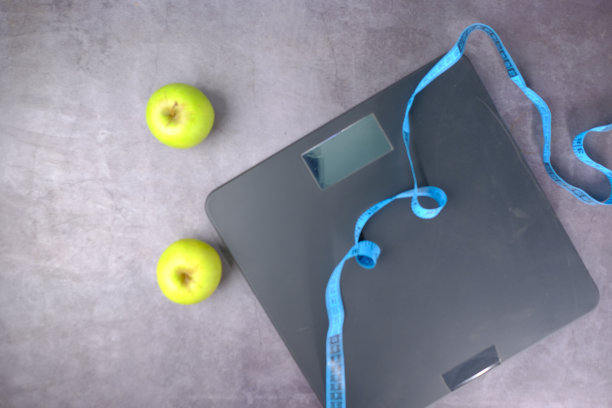 地上放着卷尺、苹果和浴室秤。图片下载