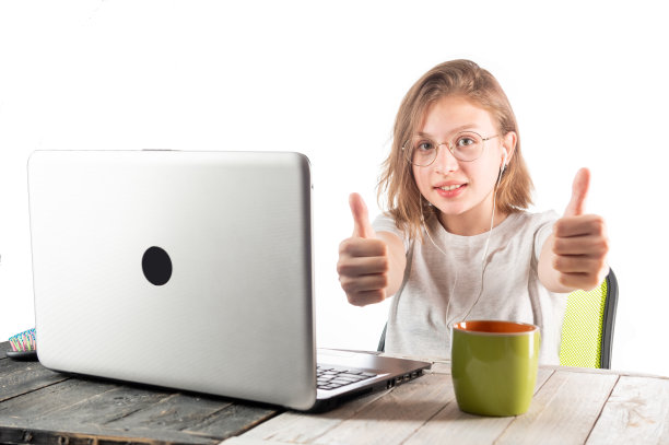 笔记本旁边有个女孩的肖像。女孩竖起大拇指。女孩祝贺。女孩很高兴。图片下载