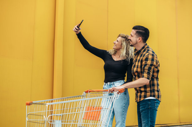 情侣们拿着超市购物车用智能手机自拍图片下载