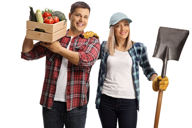 年轻的男性农民拿着一个装着蔬菜的板条箱和一个拿着铁锹的女性农民图片下载