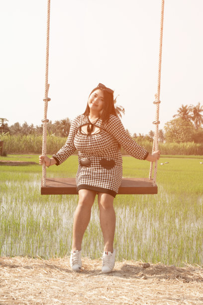一个年轻漂亮的亚洲胖女人在稻田里荡秋千。图片下载