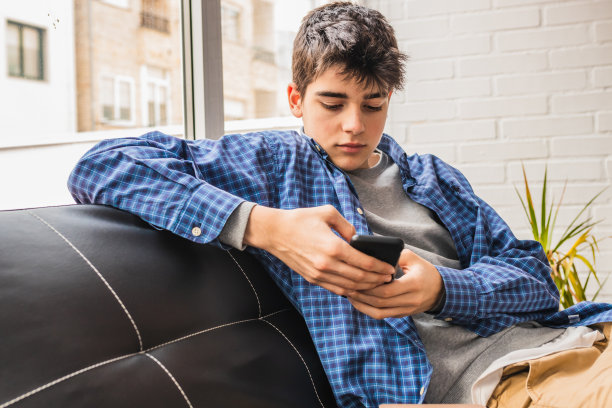 年轻的学生拿着手机和书坐在家里的沙发上图片下载