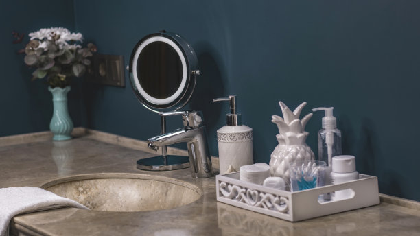 色彩新潮的浴室，洗涤区，卫生整洁。圆形金属镜，棉垫，耳棒，膏霜，液体肥皂在一个分配器。石材台面，白色毛巾。舒适的浴室内。图片下载