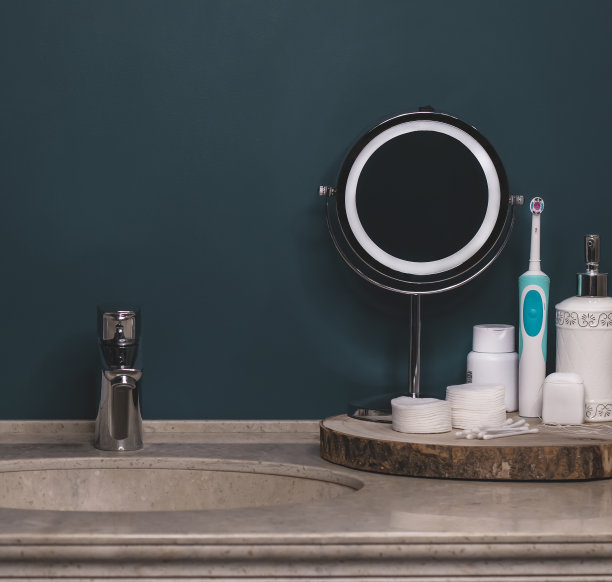 色彩新潮的浴室，洗涤区，卫生整洁。圆形金属镜，棉垫，耳棒，膏霜，液体肥皂在一个分配器。石材台面，白色毛巾。舒适的浴室内。图片下载