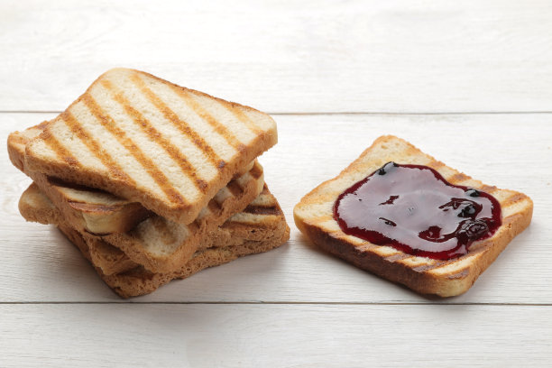 烤面包片和果酱。白色的木桌上放着涂着红果酱的酥脆吐司。图片下载