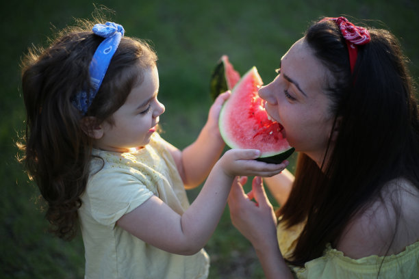 可爱的女儿和妈妈在夏天吃西瓜。公园里的快乐女孩。库存图片图片下载