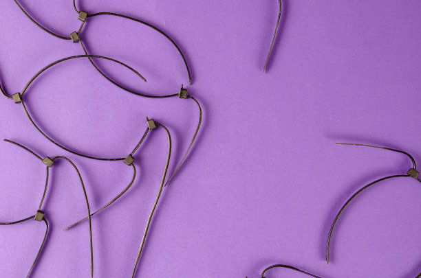 黑色的铁丝系在淡紫色的背景上。旧剪塑料领带。图片下载