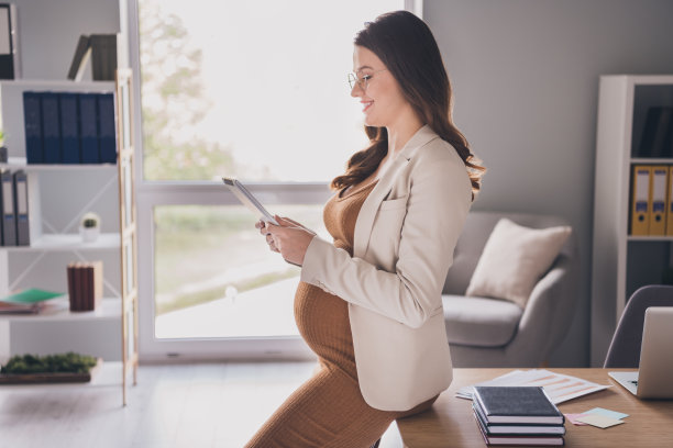 照片肖像侧面侧面的孕妇抱着平板电脑坐在桌子上在现代办公室图片下载