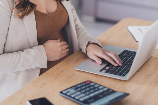 照片肖像裁剪顶部高角度的观点，孕妇工作在笔记本电脑打字坐在办公桌在现代办公室图片下载