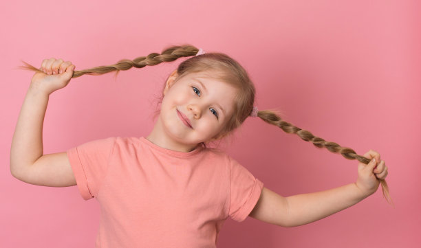 粉红色背景上扎着辫子的小女孩的肖像。图片下载