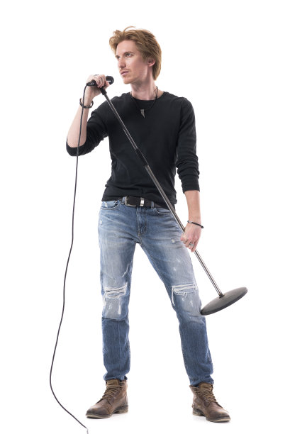 英俊的歌手在牛仔裤拿着麦克风摆姿势和看别处。图片下载