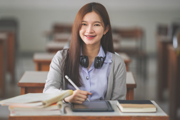 这是一名年轻的亚洲女大学生在大学教室里穿着学生制服在笔记本上学习和写作的照片图片下载