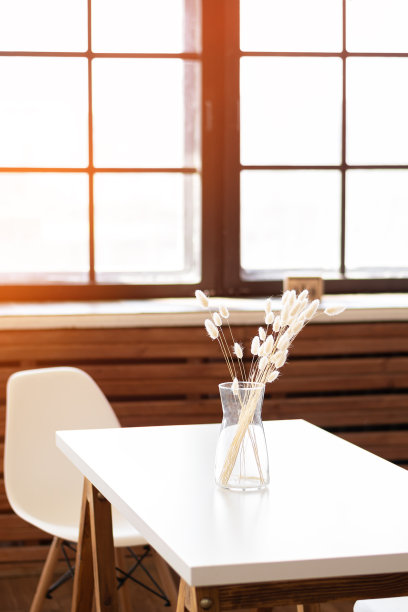 干花放在白色桌子上的玻璃罐里。闪亮的窗户前的桌子上，花瓶里插着白色的干花。图片下载