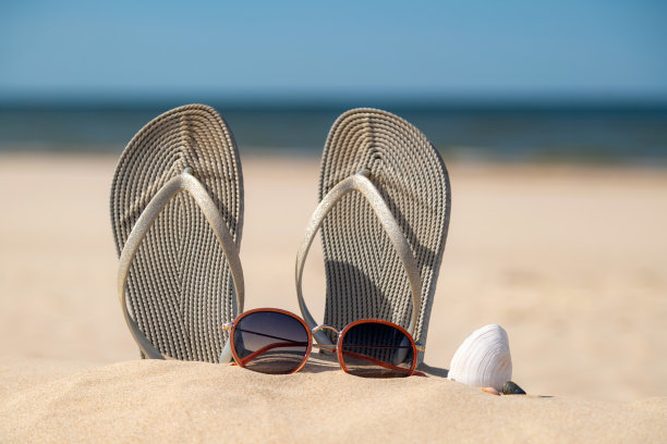 在一个美丽的阳光明媚的日子里，沙滩上穿着灰色的凉鞋。拖鞋在海边的沙滩上。人字拖在海边。图片下载
