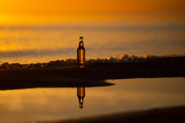 一个冰镇的啤酒/汽水瓶子，在夕阳的金色沙滩上挺立。夏天的晚上图片下载