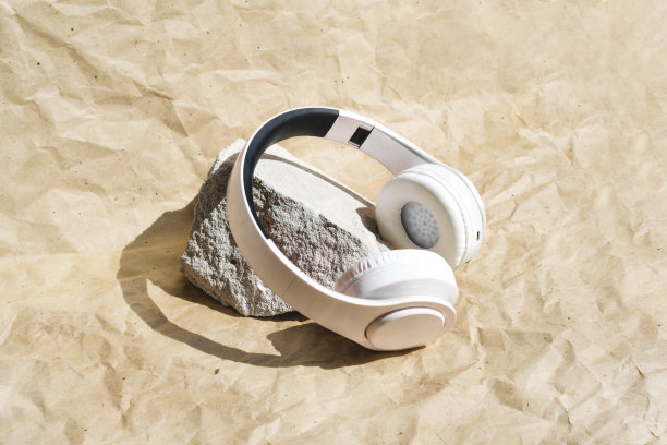 白色无线耳机，米色牛皮纸背景。灰色石头展柜上的便携式音乐设备图片下载