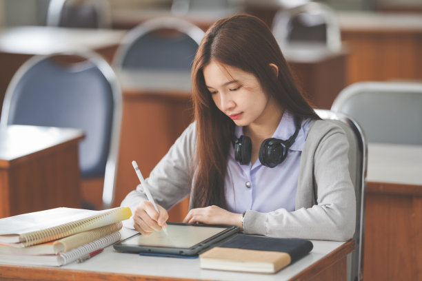 这是一名年轻的亚洲女大学生在大学教室里穿着学生制服在平板电脑上学习和写作的照片图片下载