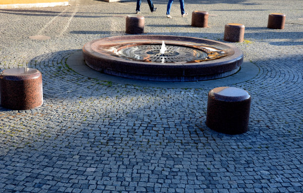 圆形喷泉抛光花岗岩棕色到红色花岗岩。广场上有石凳和鹅卵石瓷砖。该喷泉是基于一个不锈钢格栅图片下载