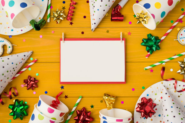 上面的照片杯子盘、五彩纸屑、生日帽、派对、小管子、哨子、蝴蝶结、请帖、纸孤立在黄色的木制背景上图片下载