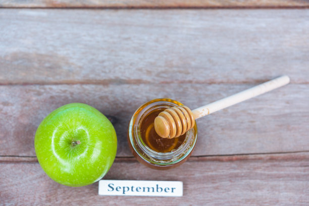 犹太节日，苹果节，在照片上有蜂蜜在罐子里，并把蜂蜜滴在绿色背景的木头上的青苹果上图片下载