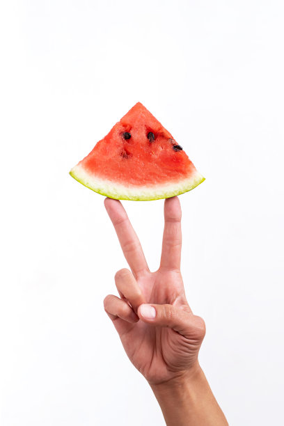 红西瓜片和女手，手势和平手势。创造性的夏天的概念。白色背景上的夏季水果成分极少。图片下载