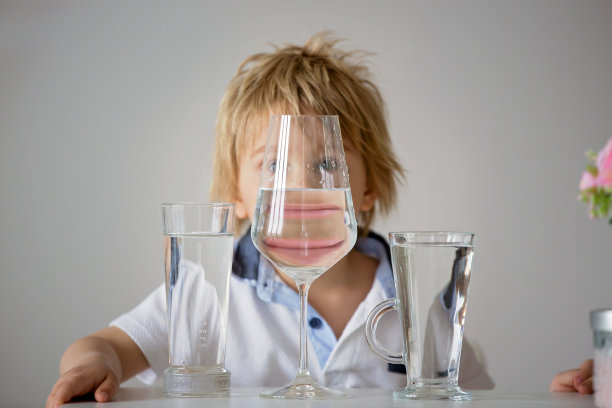 倒影着一个可爱的小男孩，笑着泡在一杯水里，滑稽扭曲着水，孩子笑了图片下载