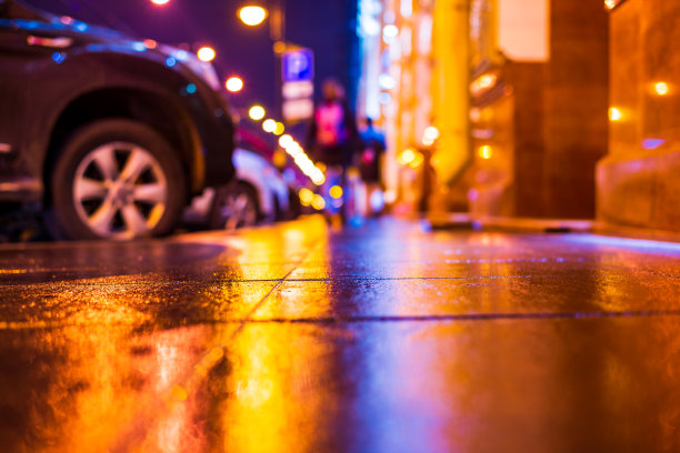 秋雨夜城。大街上有很多人。停着的汽车。商店橱窗里的灯光反射在人行道上。图片下载