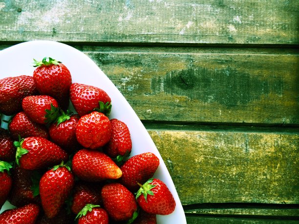 盘子上放草莓，木制背景。白色的菜肴和美味的红色大花园草莓。健康的食物，维生素和素食。有食物的静物。副本的空间。平躺图片下载