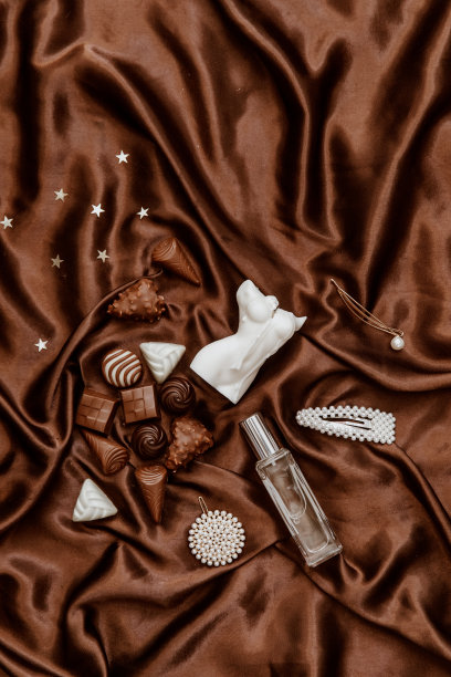 风格平铺珠宝，巧克力糖果，女人身材蜡烛在棕色丝绸背景。生活方式，美容概念博客，社交媒体，杂志。图片下载