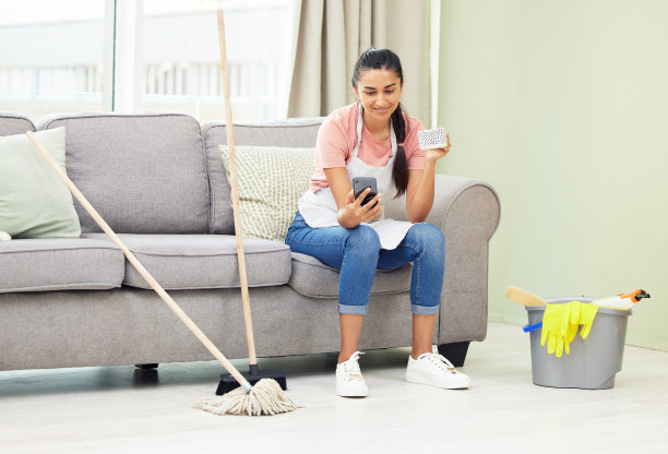 这张照片拍摄的是一个女人在打扫房间休息的时候用手机喝咖啡图片下载