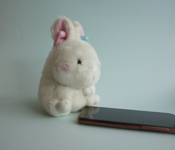 一只白色的玩具兔子戴着耳机，旁边是蓝色背景的智能手机图片下载