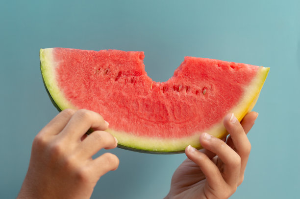 近距离的一块西瓜，用手咬了一口，在一个清晰的夏季蓝色背景。图片下载