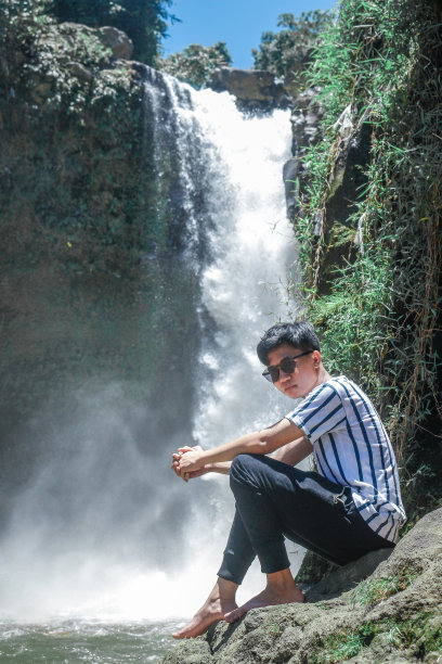 一个年轻人坐在森林里的瀑布附近图片下载