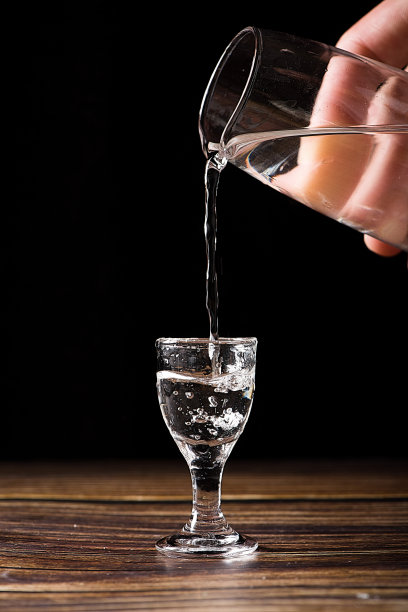 中国白酒，烈酒饮料从一个瓶子倒进一个玻璃杯的木材背景图片下载