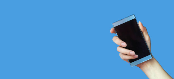 女人的手拿着手机与空白屏幕上的蓝色孤立背景。你广告的概念模型。特写，拷贝空间，横幅图片下载