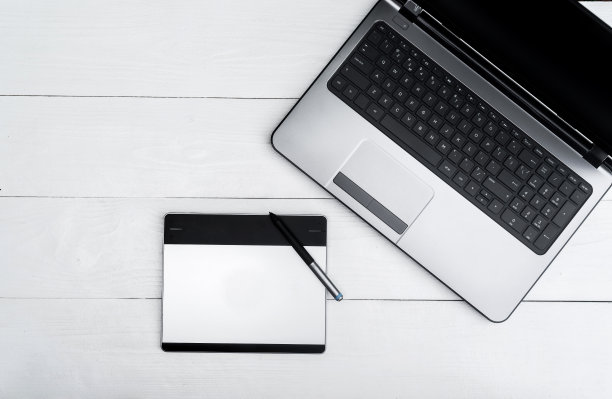 木质的白色办公桌桌上有打开的空白笔记本电脑和图形板，自由的空间。顶部视图与复制空间。灰色笔记本电脑与图形平板木桌子的背景图片下载